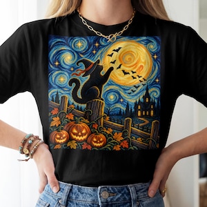 May include: A black t-shirt featuring a graphic print of a black cat wearing a witch hat sitting on a fence, reaching toward a flock of bats against a swirling yellow moon, starry blue sky, a dark house, and three glowing orange jack-o'-lanterns.