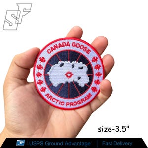 May include: A circular embroidered patch measuring 3.5 inches in diameter. The patch features a dark blue center with a white map graphic and a red sunburst icon, surrounded by a white border with red maple leaves and the text CANADA GOOSE ARCTIC PROGRAM.