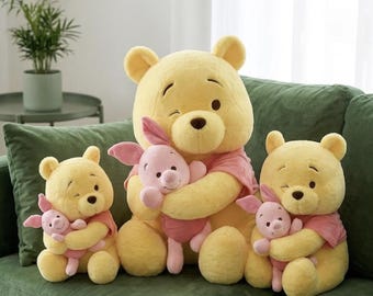 May include: Three yellow plush bears, each wearing a pink shirt and holding a small pink plush piglet. The central bear is larger than the two identical smaller bears positioned on either side. All figures have embroidered facial features.