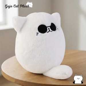 May include: A white plush cat toy with a rounded body, pointed ears, and a small tail. The cat features embroidered black sunglasses, a simple nose, and whiskers. The text Gojo Cat Plush is visible in the upper left corner of the image.