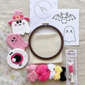 May include: A punch needle craft kit featuring a dark wood embroidery hoop, a piece of beige fabric, a punch needle tool in packaging labelled HELLO PUNCH NEEDLE, five yarn bundles in pink, white, yellow, and black, and three finished felted patches.