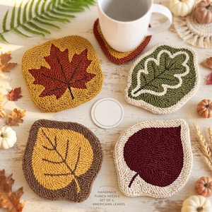 Könnte beinhalten: Ein Set aus vier Punch-Needle-Untersetzern in Blattform mit herbstlichen Farben wie Rot, Gelb, Grün und Braun. Das Set enthält ein quadratisches Ahornblatt, ein Eichenblatt und zwei abgerundete Blattformen. Text: HANDMADE PUNCH NEEDLE SET OF 4, AMERICANA LEAVES.