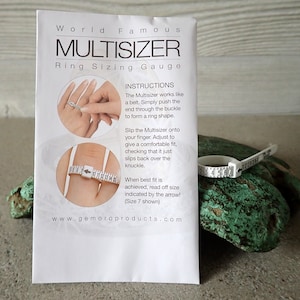 May include: White plastic ring sizer with a numbered scale from 2 to 7. The sizer is wrapped around a finger and the arrow points to the size 7 mark. The instructions on the white paper card say "World Famous Multisizer Ring Sizing Gauge".