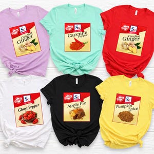 May include: Six short-sleeve crew neck t-shirts in lavender, mint green, red, white, black, and yellow. Each shirt features a square graphic print resembling a spice jar label with text including Candied Ginger, Cayenne Pepper, Ghost Pepper, Apple Pie Spice, and Pumpkin Spice.