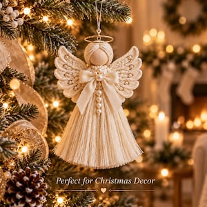 Può includere: Un ornamento a forma di angelo in macramè con una testa in perla di legno liscia, un'aureola in filo dorato e ali in corda color crema. Il corpo è realizzato in corda sfrangiata con una fila centrale di perline bianche e un fiocco in raso.