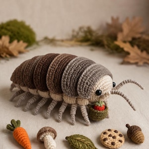 May include: A crocheted pill bug toy with a segmented brown and gray body, black eyes, and antennae. It holds a small green basket containing a red strawberry. Nearby are crocheted items: an orange carrot, a mushroom, a leaf, a cookie, and an acorn.