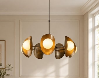 Op de afbeelding: Een ronde kroonluchter met een centrale stang en meerdere armen die naar buiten steken. Elke arm heeft een matte, messingkleurige, schelpvormige kap die een bolvormige, matwitte gloeilamp gedeeltelijk omsluit voor warm licht.