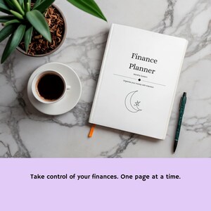 Puede incluir: Un planificador financiero blanco con un dibujo lineal negro de una luna creciente y una estrella en la portada. El texto dice Finance Planner, Monthly System y Organize your money with intention. Un bolígrafo verde oscuro está junto al planificador.