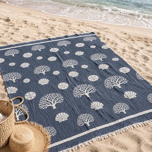 Op de afbeelding: Een rechthoekige marineblauwe strandhanddoek met een herhalend wit patroon van koraaltakken en schelpen. De handdoek heeft een effen marineblauwe rand met dunne witte strepen en korte, gerafelde franjes aan de twee korte zijden.