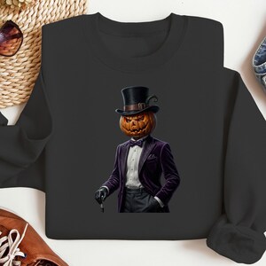 May include: A black long-sleeve sweatshirt featuring a graphic print of a pumpkin-headed figure wearing a black top hat, a purple velvet tuxedo jacket, a white dress shirt, a black bow tie, and black gloves, while holding a small black cane.