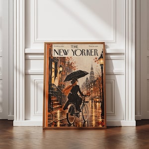 Peut inclure: Une impression encadrée de la couverture du magazine The New Yorker datée du 31 octobre 2024. L'illustration montre une personne en manteau noir et écharpe orange à vélo avec un parapluie dans une rue urbaine avec des feuilles d'automne.