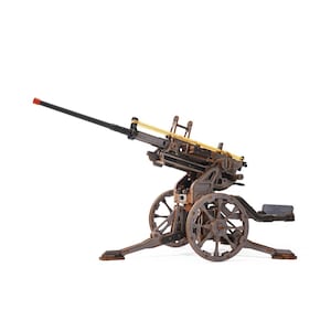 May include: A brown wooden model of an anti-aircraft gun featuring a long barrel with a red tip, a mechanical gear system, spoked wheels, and yellow rubber bands attached to the top mechanism, all mounted on a stable tripod base structure.
