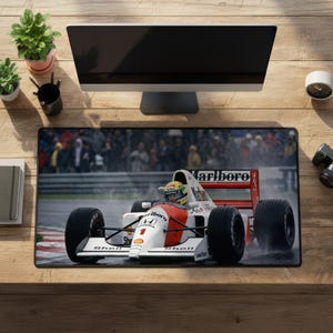 Peut inclure: Un tapis de bureau rectangulaire présentant une photographie haute résolution d'une voiture de Formule 1 blanche, rouge et noire portant le numéro 1, les logos Marlboro, Honda et Shell, roulant sur une piste mouillée avec une foule floue.