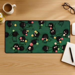 May include: A rectangular desk mat featuring a dark green background with a repeating pattern of small, round, black, fuzzy creatures with large eyes. The creatures are holding various pastel-colored star-shaped objects in pink, yellow, and light green.