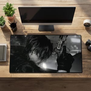 Puede incluir: Una alfombrilla de escritorio rectangular con un estampado gráfico en blanco y negro de una persona con cabello oscuro sosteniendo una pistola. La alfombrilla está sobre una mesa de madera frente a un monitor, una planta y un reloj.