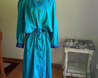 May include: A teal blue long-sleeved jacket with a matching skirt. The jacket has a high collar, button closure, and a drawstring waist. The skirt has a button closure and pockets.