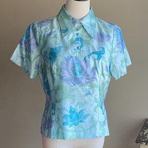May include: A light blue short-sleeved blouse with a floral print. The print features blue, purple, and green flowers on a light blue background.