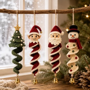 Op de afbeelding: Vier gehaakte kerstornamenten hangen aan een houten tak. De ornamenten bestaan uit een groene boom met een gele ster, een elf met een rode muts, een kerstman met een witte baard en een sneeuwpop met een zwarte hoed en rode sjaal, elk met een belletje.