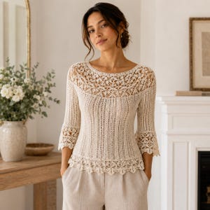 May include: A cream-colored knit top featuring a delicate floral lace pattern around the neckline, hem, and three-quarter length sleeves. The bodice displays a vertical ribbed texture, while the edges are finished with a scalloped crochet design.