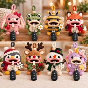 May include: Eight crocheted animal key pouches with open mouths holding black car key fobs. The characters include a pink rabbit, green frog, yellow bee, orange fox, penguin, reindeer, snowman, and purple unicorn, each with a hanging loop.