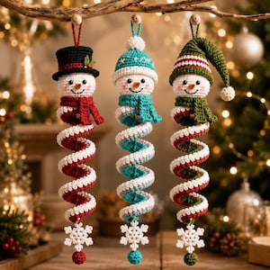 May include: Three hanging crochet snowman ornaments with spiral bodies. The left snowman wears a black top hat and red scarf. The center snowman has a turquoise beanie and scarf. The right snowman wears a green striped hat and scarf. Each ends in a white snowflake.