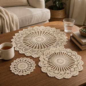 May include: A set of three round, cream-colored crochet doilies featuring intricate, radiating patterns with scalloped edges. The collection includes one large doily, one medium doily, and one small doily, all crafted with fine thread in a circular design.