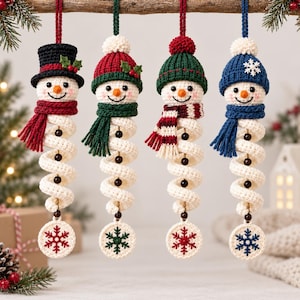 Könnte beinhalten: Vier gehäkelte Schneemann-Ornamente hängen in einer Reihe. Jeder Schneemann hat einen weißen spiralförmigen Körper, eine bunte Mütze, einen passenden Schal und eine runde Basis mit Schneeflockenmuster sowie kleinen dunklen Perlen verziert.