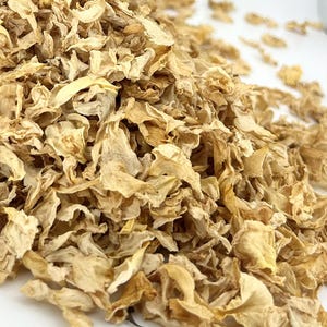 May include: A large pile of dried, light yellow flower petals with a crinkled, delicate texture. The petals vary in shade from pale cream to golden yellow, showing natural organic shapes and curled edges scattered across the frame.