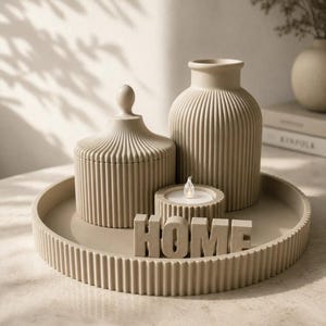 Peut inclure: Un ensemble décoratif beige comprenant un plateau rond cannelé, un pot à couvercle cannelé, un grand vase cannelé, un petit bougeoir circulaire avec une bougie chauffe-plat blanche et des lettres formant le mot HOME en ton beige assorti.