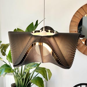 Peut inclure: Une suspension en forme d'étoile avec une texture sombre, superposée et ondulée. La lampe possède une source lumineuse blanche centrale et est suspendue par un cordon blanc unique. La structure se compose de cinq sections pointues.