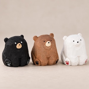 May include: Three small carved bear figurines in a seated position. The left bear is black with grey paw pads, the centre bear is brown with black paw pads, and the right bear is white with red paw pads. Each bear has a faceted, textured surface.