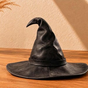 Puede incluir: Un sombrero puntiagudo de color negro con ala ancha y una copa estructurada ligeramente curvada. El sombrero presenta un acabado mate y liso, con una banda negra a juego que rodea la base de la copa, creando una silueta distintiva y cónica.
