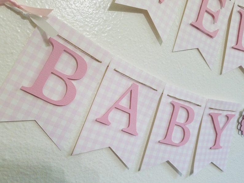 以下が含まれることがあります： ピンクと白のギンガムチェックのバナーで、ピンクの文字で「BABY」と書かれています。バナーは紐でつながれており、上部にピンクのリボンが付いています。ベビーシャワーや保育園の装飾に最適です。