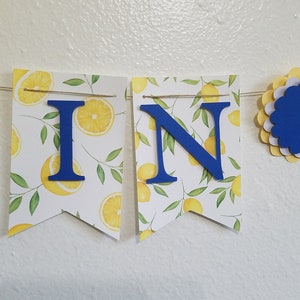 May include: A yellow and white lemon-themed banner with blue letters spelling "WIN" and blue and yellow paper rosettes.