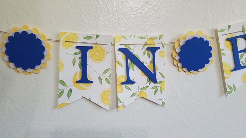 May include: A yellow and white lemon-themed banner with blue letters spelling "WIN" and blue and yellow paper rosettes.
