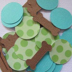 May include: A collection of paper cutouts in various shapes and colors. There are light green circles with green polka dots, teal circles, and brown bone shapes. The cutouts are scattered across a white surface.