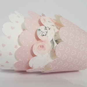 May include: A set of three pink and white cupcake liners with scalloped edges. The liners feature different patterns, including hearts, polka dots, and floral designs.