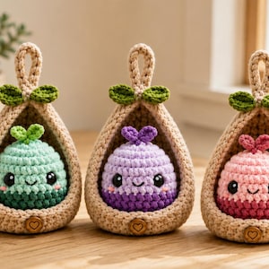 Peut inclure: Trois nacelles suspendues en crochet beige, contenant chacune une petite créature ronde et souriante avec des yeux noirs et un germe sur le dessus. Les créatures sont vert menthe, lavande et rose, avec des bases plus foncées et des boutons en bois.