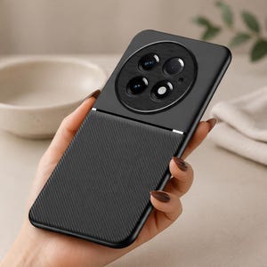 Könnte beinhalten: Eine schwarze Smartphone-Hülle mit einem großen kreisförmigen Kameramodul im oberen Bereich und einem strukturierten Muster aus diagonalen Linien im unteren Teil. Die Hülle hat eine glatte, matte Oberfläche und eine dünne silberne Zierlinie.