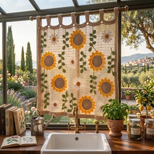 May include: A beige crochet curtain featuring a grid pattern adorned with appliqued yellow sunflowers and white daisies with green vine accents. The curtain hangs from a rod with tab tops and covers a window above a white kitchen sink.
