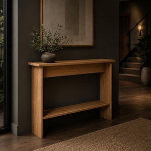 May include: A rectangular light brown wooden console table featuring a flat top surface and a lower shelf. The table is constructed with vertical side panels and a horizontal support beam beneath the top surface, showcasing a natural wood grain finish.