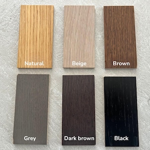 May include: Six rectangular wood veneer samples arranged in two rows. The top row features natural, beige, and brown finishes. The bottom row displays grey, dark brown, and black finishes. Each sample is labelled with its respective colour name.