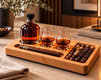 May include: A rectangular light-toned wooden serving tray featuring a recessed circular area for a glass decanter filled with amber liquid, two matching glasses with amber liquid, a long slot for a cigar, and a compartment filled with chocolates.