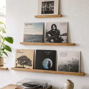Puede incluir: Tres estantes flotantes de madera clara montados en una pared blanca, exhibiendo seis portadas de discos de vinilo incluyendo Rodriguez, Ryan Adams, Neil Young, Jack Johnson, John Martyn y Vampire Weekend, sobre un tocadiscos de madera.