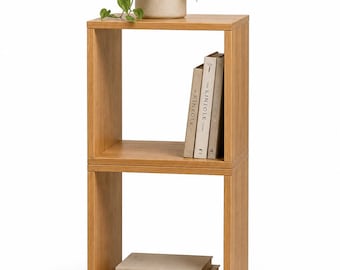May include: A light brown wooden two-tier shelving unit with a square frame. The top shelf holds a beige pot with a green plant and three books titled Kinfolk. The bottom shelf contains two stacked books, with the bottom one labeled Eat Drink Nap.