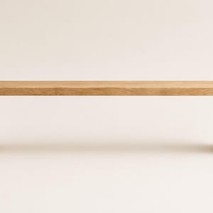 May include: A rectangular bench constructed from light-toned wood with a smooth, flat surface and two vertical side supports. The design features clean, straight lines and a natural wood grain pattern visible across the entire structure.