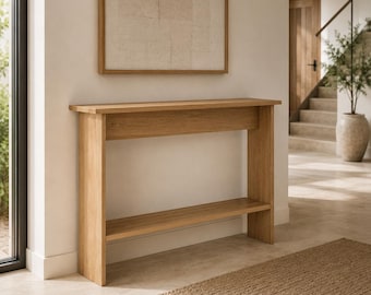 May include: A light oak console table featuring a rectangular top, a single horizontal support beam, and a lower shelf. The piece is constructed with clean, straight lines and a natural wood grain finish, standing on two flat side panels.