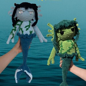May include: Two crocheted plush dolls titled Serena the Moss Siren. The left doll has light blue skin, black hair, and a dark blue tail. The right doll is green with dark green hair and a dark green tail. Both feature moss-like patterns and fins.