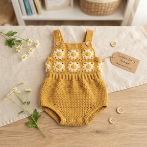 May include: A mustard yellow crochet romper featuring a square-patterned bodice with white daisy motifs and two wooden buttons at the straps. A brown paper tag attached to the side reads Golden Daisy Romper Handmade with Love.