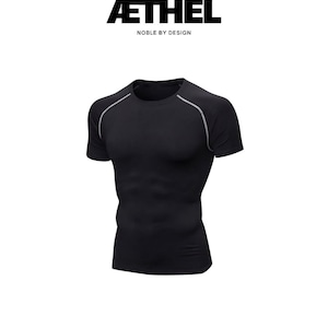 Pode incluir: Uma t-shirt de compressão preta de manga curta com decote redondo e debrum cinzento-claro ao longo das costuras das mangas raglan. Acima da t-shirt, o texto AETHEL está impresso em letras pretas, seguido pelo texto NOBLE BY DESIGN.